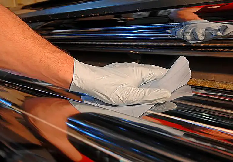 Hand mit weißem Handschuh poliert schwarze glänzende Oberfläche