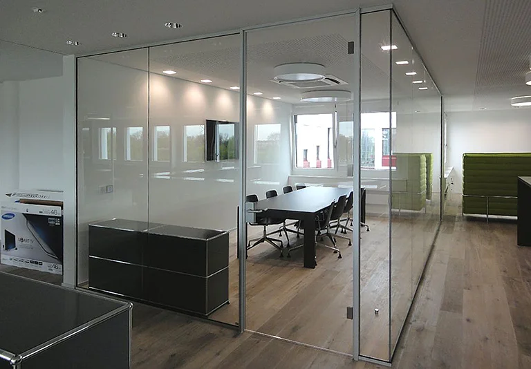 Modernes Büro mit Glastrennwänden, Konferenzraum mit schwarzem Tisch und Stühlen, Holzboden, grüne Loungemöbel