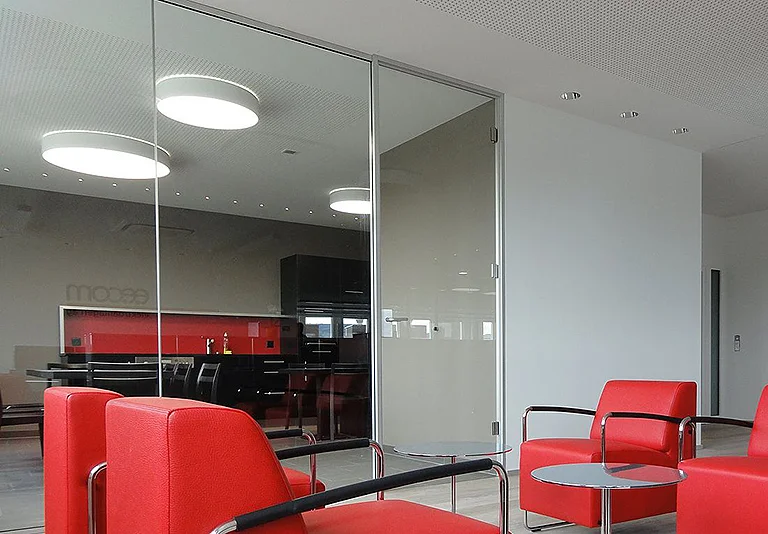 Moderner Büro-Wartebereich mit roten Ledersesseln, Glastüren und Blick auf Küchenbereich mit schwarzen Schränken