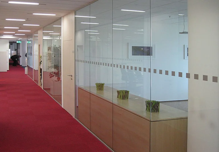 Moderner Büroflur mit rotem Teppich und Glastrennwänden zu Besprechungsräumen mit Holzmöbeln und Pflanzen