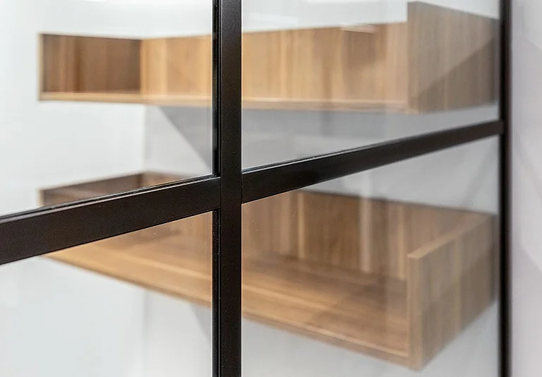Glasvitrine mit schwarzem Metallrahmen und Holzregalen in hellem Eichenholz vor weißer Wand