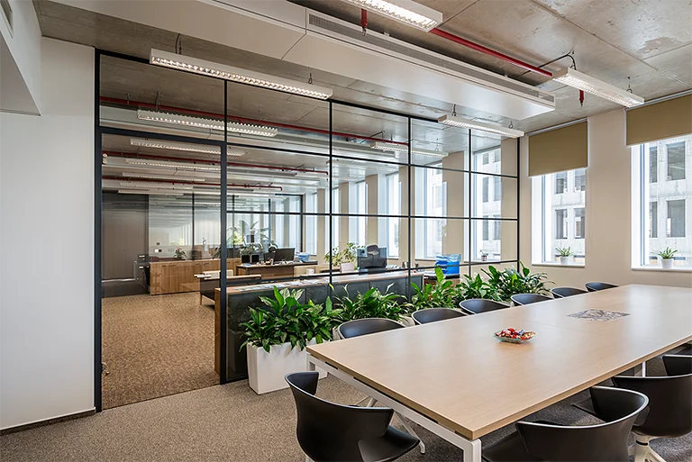 Modernes Büro mit Glastrennwänden, langem Konferenztisch mit schwarzen Stühlen und grünen Zimmerpflanzen