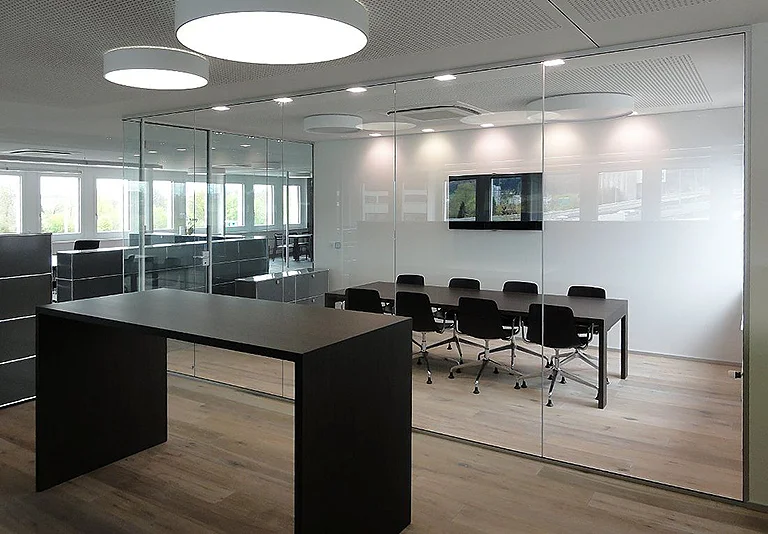 Moderner Büroraum mit Glastrennwänden, Konferenzraum mit schwarzen Stühlen und dunklem Stehtisch im Vordergrund