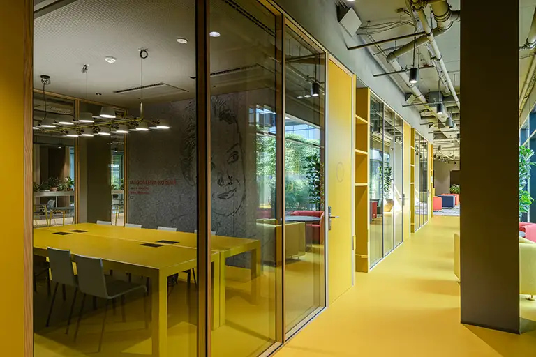 Moderne Büroräume mit gelben Glastrennwänden, Besprechungsraum mit gelbem Tisch und grauer Wandkunst
