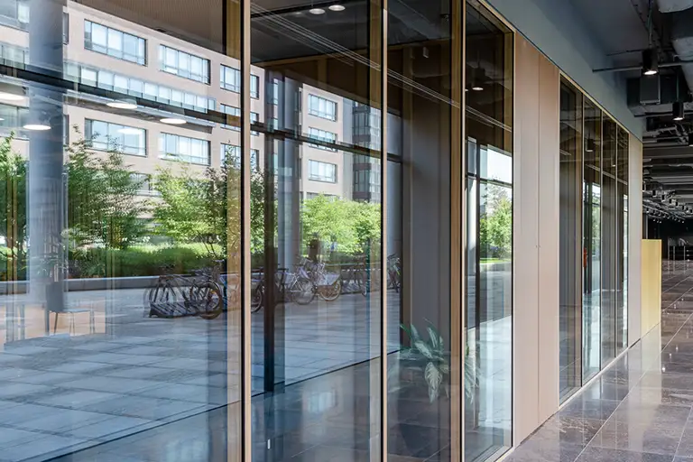 Moderne Glasfassade eines Bürogebäudes mit Blick auf begrünten Innenhof, Fahrräder und Nachbargebäude