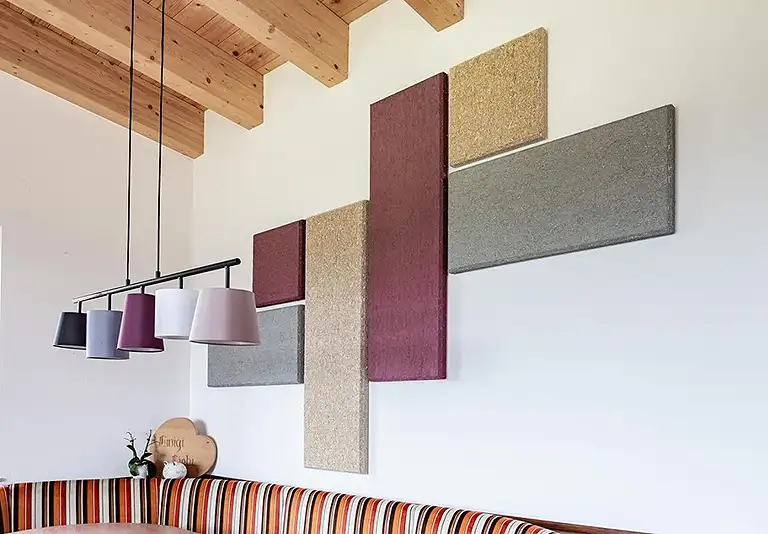 Moderne Akustikpaneele in Grau, Beige und Bordeaux an weißer Wand mit Holzbalkendecke und Pendelleuchten