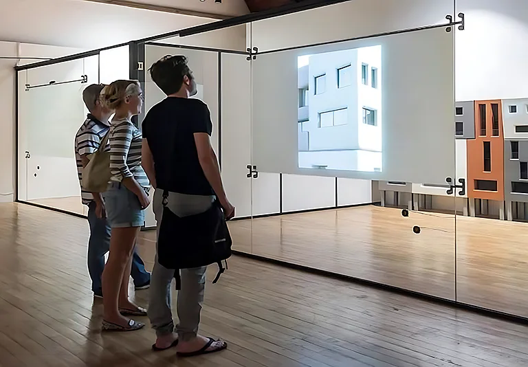 Drei Personen betrachten eine Projektion eines weißen Gebäudes in einem Ausstellungsraum mit Smart-i-Wall