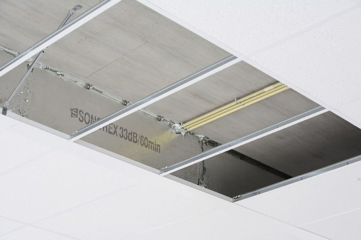 Abgehängte Decke mit entfernten Platten zeigt Rohdecke, gelbe Rohre und Schallschutzpaneele mit 33dB/60min Kennzeichnung