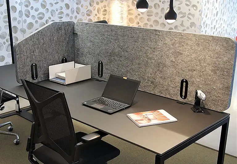 Moderner Büroarbeitsplatz mit grauem Schreibtisch, schwarzem Laptop, Akustik-Trennwänden aus Filz und ergonomischem Stuhl
