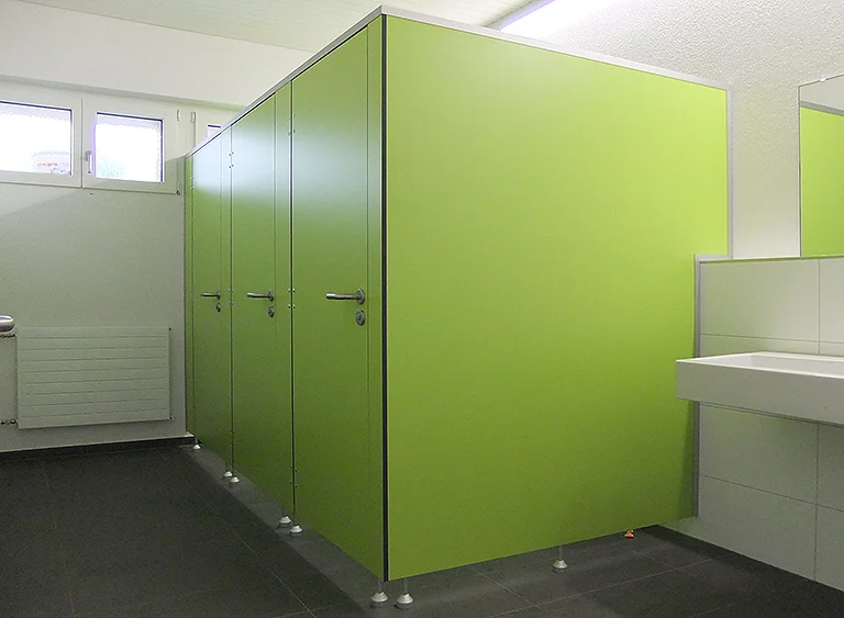 Moderne Sanitäranlage mit drei hellgrünen WC-Kabinen, dunklem Fliesenboden und weißem Waschbecken rechts