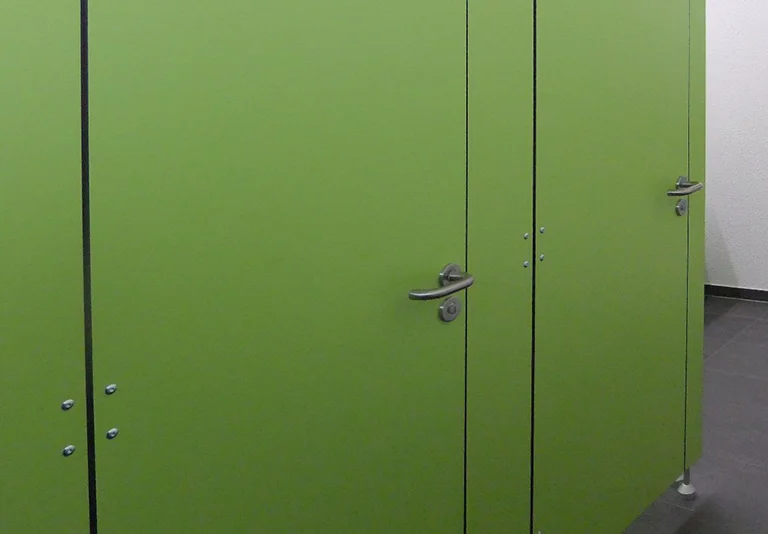 Grüne Toilettenkabinen-Trennwände mit silbernen Türgriffen und Schlössern in einem modernen Sanitärraum