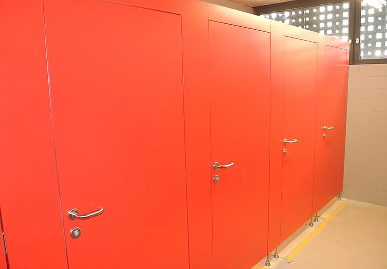 Reihe von vier orangeroten Toilettenkabinentüren mit silbernen Türgriffen in einem gefliesten Sanitärraum