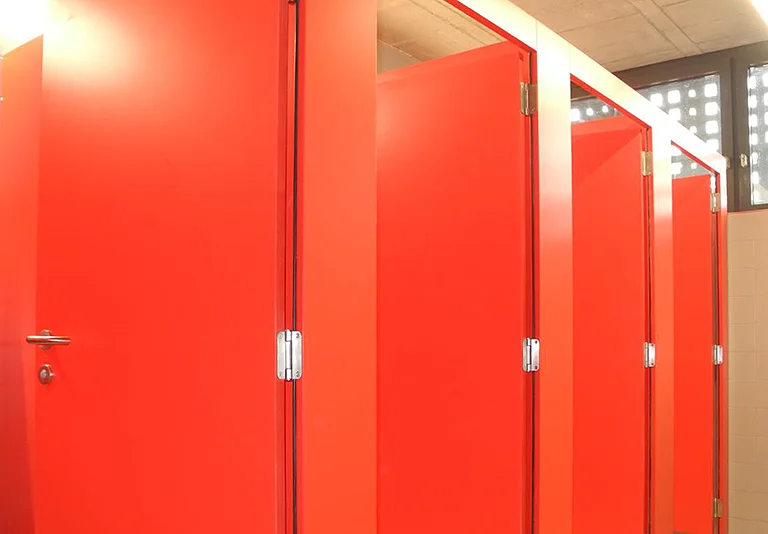 Reihe leuchtend roter Toilettenkabinen mit silbernen Scharnieren in einem öffentlichen Waschraum