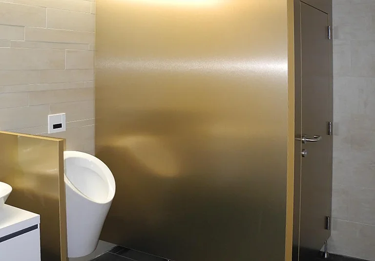 Modernes Herren-WC mit weißem Urinal, goldfarbener Trennwand und beigefarbenen Wandfliesen