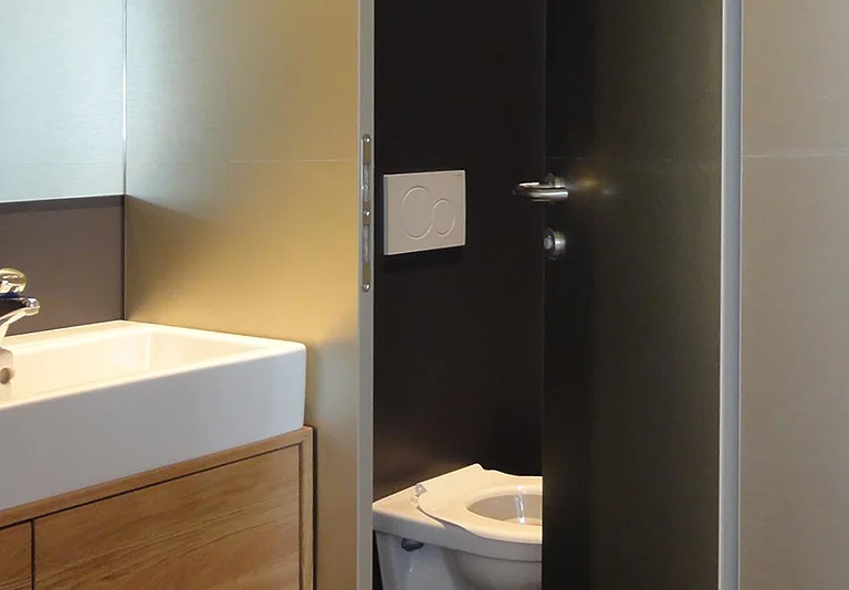 Modernes Badezimmer mit weißem Waschbecken auf Holzunterschrank, daneben separate Toilettenkabine mit dunkler Tür